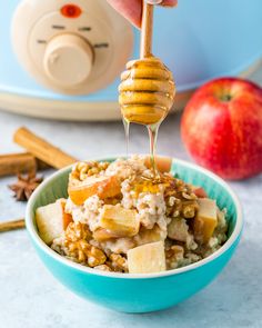 a bowl filled with oatmeal, apples and honey being drizzled over it