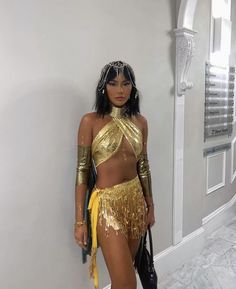 a woman in a gold outfit standing next to a wall with her hand on her hip