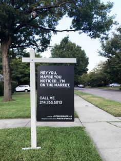 a black and white sign sitting on the side of a road next to a tree