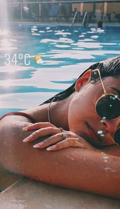 a woman wearing sunglasses laying on the edge of a swimming pool with her arms around her chest