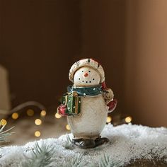 a snowman figurine on top of a pile of snow with lights in the background