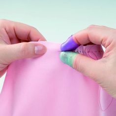 two hands are holding a piece of pink material with purple and green tips on it