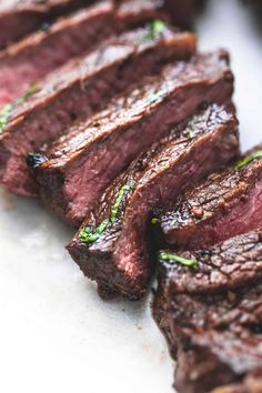 some meat is sitting on a plate with green garnish and seasoning around it