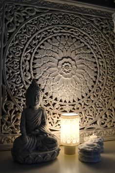 a buddha statue sitting next to a lit candle on top of a table in front of a carved wall