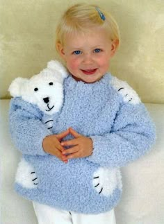 a little boy holding a teddy bear in his arms while wearing a blue knitted sweater