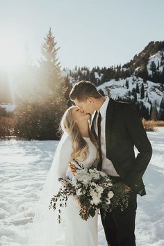 a bride and groom kissing in the snow