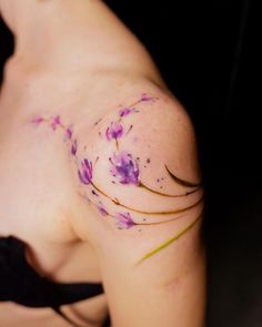 a woman with purple flowers on her arm and chest tattooing it's back