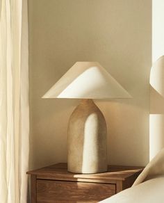 a white lamp sitting on top of a wooden table next to a bed in a bedroom