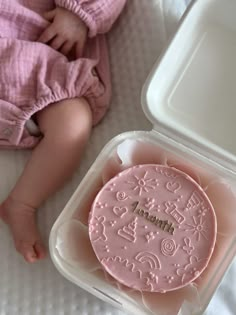 a baby laying next to a pink cake in a plastic container