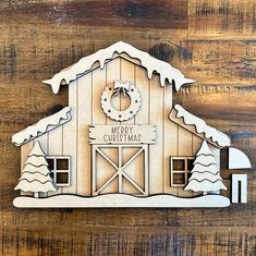 a wooden cutout of a barn with snow on the roof and wreath hanging from it