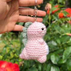 a hand holding a tiny crocheted keychain with a small pink animal hanging from it's side