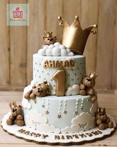 a blue and white cake with teddy bears on it's tiers, topped with a gold crown