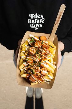 a person holding up a paper container filled with fries and toppings on top of it