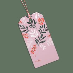 a pink gift tag with red berries and leaves on it, hanging from a string