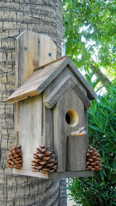 a wooden birdhouse with pine cones hanging from it's side next to a tree