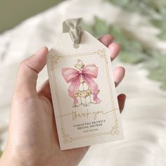 a hand holding a tag with a pink bow on it