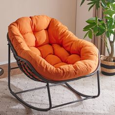 an orange chair sitting on top of a rug next to a potted plant