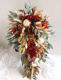 a bridal bouquet made up of flowers and leaves on a white cloth covered table