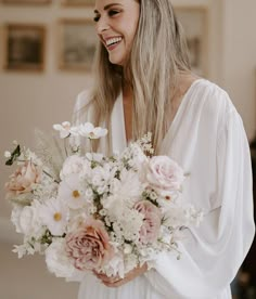 a woman holding a bouquet of white and pink flowers in her hands smiling at the camera