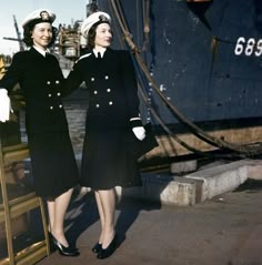 two women in uniform standing next to each other near a boat on the water,