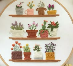 some potted plants and flowers are on the shelves in this embroidery pattern that is hanging on a wall