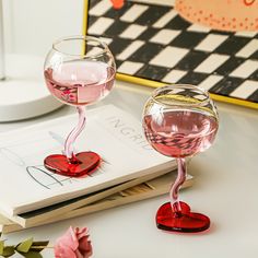 two wine goblets sitting on top of a table next to a book and flowers