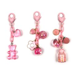 three pink key chains with various charms attached to them, one has a teddy bear and the other has an apple