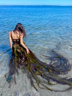 a woman is sitting in the water with her long dress on