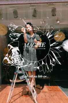 a woman standing on a stepladder in front of a window with the words magpie painted on it