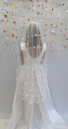 the back of a bride's wedding dress with flowers flying from her head and veil