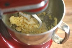 a red mixer filled with food on top of a wooden table