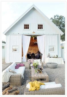 a group of people standing in front of a white barn with lots of furniture and decor