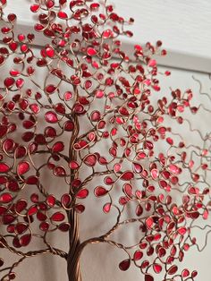 a metal tree sculpture with red glass hearts on it's branches, hanging from a white wall