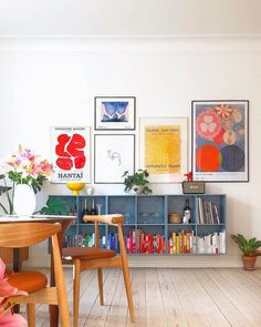 there are many pictures on the wall above the table in this living room with chairs and bookshelves