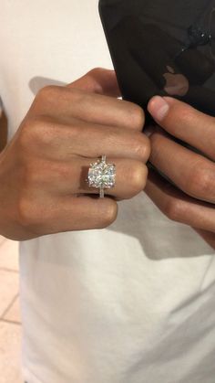 a woman is holding her cell phone and wearing a ring with a princess cut diamond on it