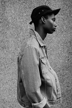 a black and white photo of a young man wearing a denim jacket, cap and jeans