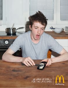 a young man sitting at a table with a cell phone in his hand and an ad for mcdonald's