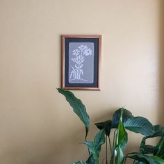 a potted plant sitting in front of a wall with a framed picture on it