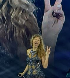 the woman is singing on stage with her hand up in front of her and two hands behind her