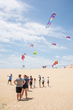 many people are flying kites in the sky at the beach on a sunny day