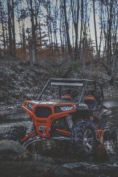 an orange polaris rzr is driving through some mud and water in the woods