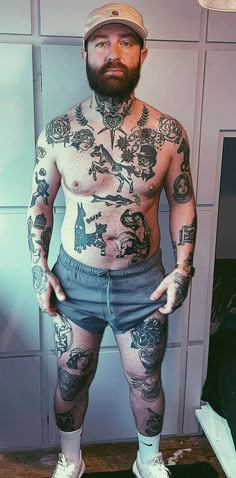 a man with tattoos on his body standing in front of a wall and wearing shorts