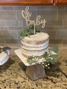 a cake with greenery on top sitting on a counter next to a wooden sign that says oh baby