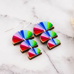 the multicolored fan shaped earrings are on top of a marble table next to a flower