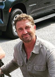 a man sitting on the ground next to a parked car and holding onto his bike