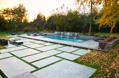 a backyard with a pool surrounded by grass and lights in the evening time, as well as lounge chairs