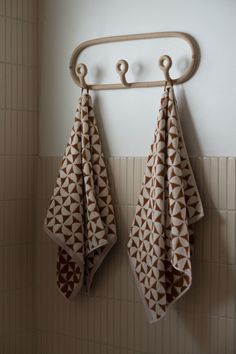 two towels hanging on a towel rack next to a white tiled wall with brown geometric designs