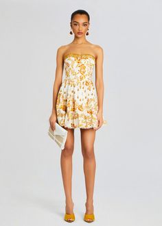 a woman wearing a yellow and white dress with an orange flower print on the front