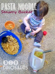 a toddler sitting on the floor playing with pasta noodles and other food items in bowls