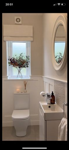 a white toilet sitting next to a bathroom sink under a window with a flower vase on top of it